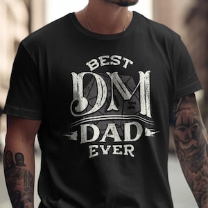 May include: Black t-shirt with white text that reads "Best DM Dad Ever" with a stylized image of a 20-sided die.