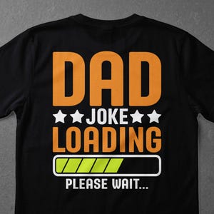 May include: Black t-shirt featuring the text "DAD JOKE LOADING" in orange and white. The design includes stars and a loading bar graphic, with the words "PLEASE WAIT..." underneath.