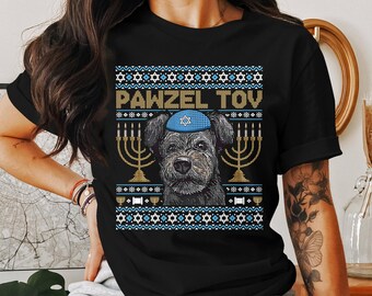 May include: Black t-shirt with a graphic featuring a dog wearing a blue yarmulke, surrounded by menorahs and a patterned design. The text "PAWZEL TOY" is displayed above the dog.