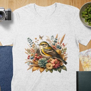 May include: A white t-shirt with a yellow and green bird perched on a bouquet of flowers. The flowers are a mix of pink, purple, blue, and yellow. The bird is surrounded by leaves and branches.