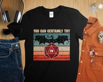 May include: Black t-shirt featuring a vintage-style graphic of a dragon and a twenty-sided die. The text "You Can Certainly Try" is printed above the graphic.