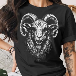 May include: Black t-shirt featuring a detailed white illustration of a ram's head. The ram has large, curved horns and a menacing expression. The design is centered on the shirt, creating a bold statement.