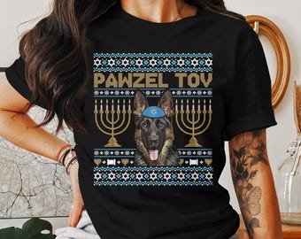 May include: Black t-shirt with a festive design featuring a German Shepherd wearing a blue yarmulke, flanked by golden menorahs. The text "PAWZEL TOV" is displayed above the dog, with a blue and white pattern.