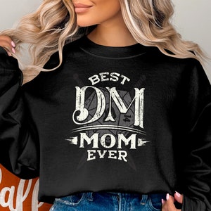 Puede incluir: Sudadera negra con texto blanco que dice "Best DM Mom Ever" con un gráfico de dados estilizado.