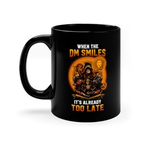 Peut inclure: Mug en céramique noire avec un graphique d'une personne en robe à capuche tenant des dés. Le texte dit "When the DM Smiles It's Already Too Late".