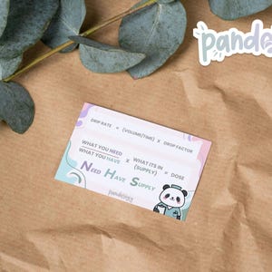 May include: A colorful card with the text "Drip Rate" and mathematical formulas. The card also features the text "Need Have Supply" and a cartoon panda illustration. The background is brown paper with eucalyptus leaves.