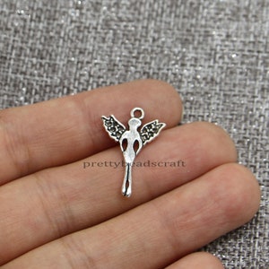 May include: Silver angel charm with wings and a loop for attaching to jewelry or crafts. The angel is standing with its wings spread out.