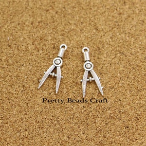 May include: Two silver compass charms with a detailed design. The charms are perfect for jewelry making or adding a unique touch to crafts.