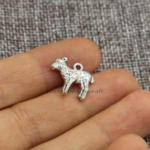 May include: Silver charm in the shape of a lamb. The charm has a detailed textured surface and a loop for attaching to a necklace or bracelet.