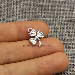 May include: Silver-toned metal charm shaped like a four-leaf clover. The charm has a loop at the top for attaching to jewelry or other crafts.