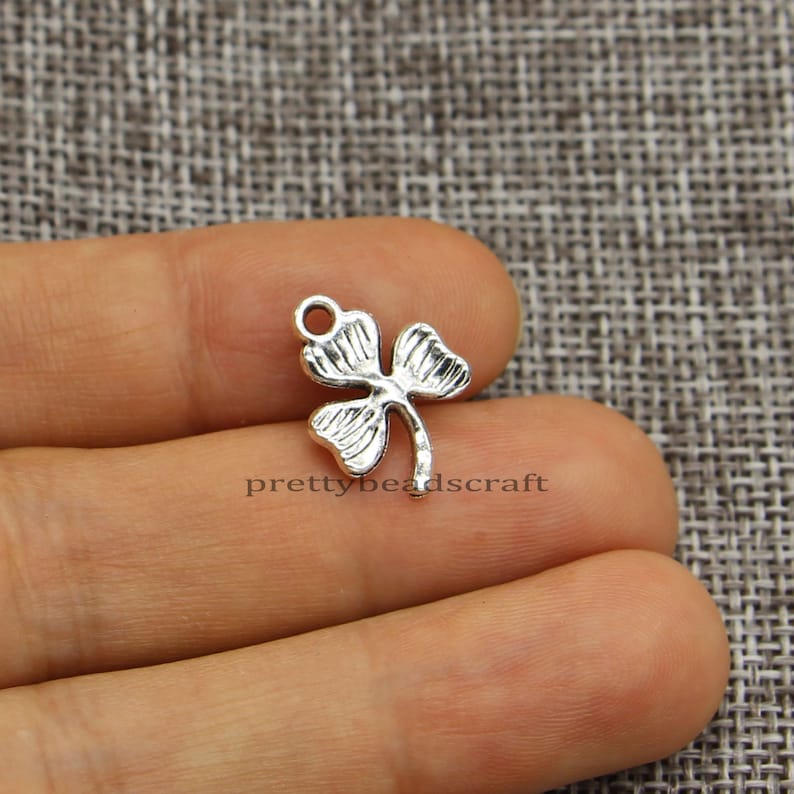 May include: Silver-toned metal charm shaped like a four-leaf clover. The charm has a loop at the top for attaching to jewelry or other crafts.
