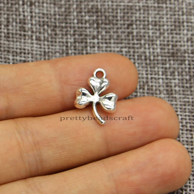 May include: Silver-toned metal charm shaped like a four-leaf clover. The charm has a loop at the top for attaching to jewelry or other crafts.