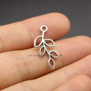Op de afbeelding: Zilverkleurige metalen bedel met een delicate tak met vijf bladeren. De bedel heeft een lus aan de bovenkant om aan sieraden of andere knutselwerken te bevestigen.