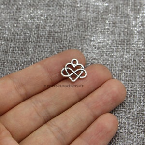 May include: Silver charm in the shape of an infinity symbol intertwined with a heart. The charm has a loop at the top for attaching to a necklace or bracelet.