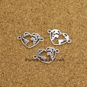 May include: Three silver-coloured heart-shaped charms with a world map design. Each charm has two loops for attaching to other jewellery components. The text "Pretty Beads Craft" is visible.