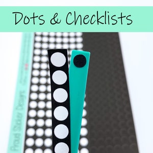 May include: Two strips of black and white dot stickers and a turquoise strip with a black dot sticker. The strips are on a black and white background with a pattern of dots.