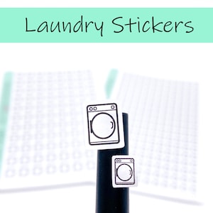 May include: Two white laundry sticker sheets with a black outline of a washing machine on each sheet. The stickers are on a black pen.