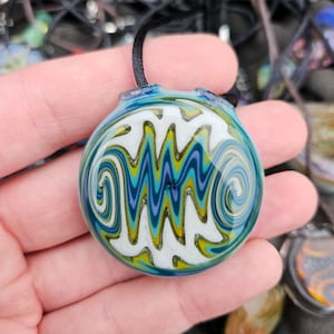 May include: A round glass pendant with a swirling pattern of white, blue, green, and gold. The pendant is attached to a black cord.