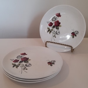 May include: Set of four white ceramic dessert plates with a floral design featuring red and white roses. The plates have a slightly raised rim and a glossy finish.