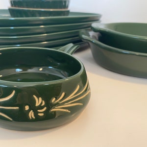 May include: A set of green ceramic dishes with a white floral design. The dishes include a large oval baking dish, a smaller round dish, and a set of four plates.