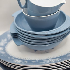 Op de afbeelding: Een stapel blauwe en witte keramische borden met een bloemenpatroon. De borden zijn op elkaar gestapeld, met een blauwe keramische kan bovenop.