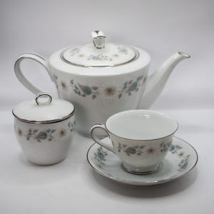 May include: A white tea set with a floral pattern. The set includes a teapot, a sugar bowl, and a teacup and saucer.