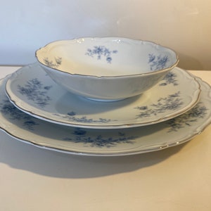 May include: A set of three white porcelain plates with a blue floral pattern. The plates are stacked on top of each other, with the smallest plate on top. The plates have a scalloped edge and a gold trim.
