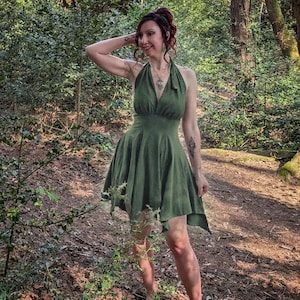 May include: A sleeveless olive green dress featuring a halter neckline with a tie closure at the back of the neck, a fitted bodice, and a short, flared skirt with an asymmetrical hemline that falls above the knees.