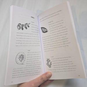 Woman holding open Medusa's grimoire book to a page that shows snake symbolism.