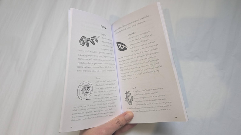 Woman holding open Medusa's grimoire book to a page that shows snake symbolism.