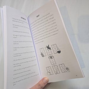 Woman holding open Medusa's grimoire book to a page showing a Medusa themed tarot card spread.