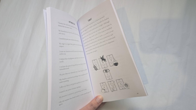 Woman holding open Medusa's grimoire book to a page showing a Medusa themed tarot card spread.