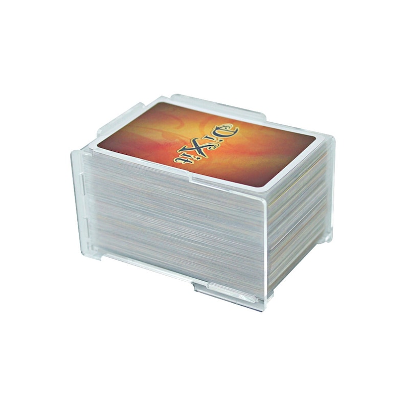 K&ouml;nnte beinhalten: Ein transparenter Kartenhalter aus Kunststoff mit einem Deck Dixit-Karten. Die oberste Karte zeigt einen feurigen orange-gelben Hintergrund mit dem Wort "Dixit" in Schwarz.