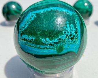 May include: A green and blue malachite sphere on a clear stand. The sphere has a swirling pattern of green and blue.