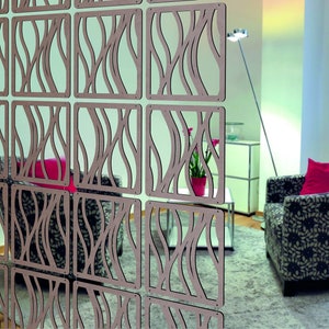 May include: A room divider made of wood panels with a decorative cut-out design. The panels are arranged in a grid pattern and feature a wavy, organic design. The divider is shown in front of a chair with a red cushion and a patterned fabric.
