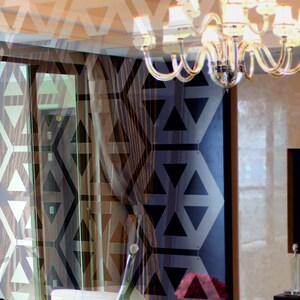 May include: A modern interior design with a large window and a chandelier with crystal accents. The room features a geometric pattern on the wall and a dark wood floor.