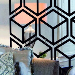 May include: A black geometric room divider with a honeycomb pattern. The divider is made of metal and has a modern design. It is shown in front of a couch with pillows.