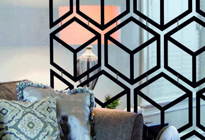 May include: A black geometric room divider with a honeycomb pattern. The divider is made of metal and has a modern design. It is shown in front of a couch with pillows.