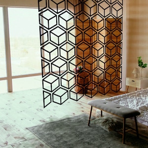 May include: A bedroom with a bed, a wooden stool, a wooden bench, and a room divider with a geometric pattern. The room divider is made of black metal and has a geometric pattern of cubes. The room is decorated with a rug, a plant, and a lamp.