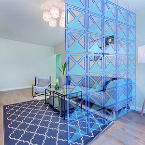 May include: A light blue room divider with a geometric pattern. The divider is made of acrylic panels and is hung from the ceiling. The divider is in front of a couch and a coffee table.