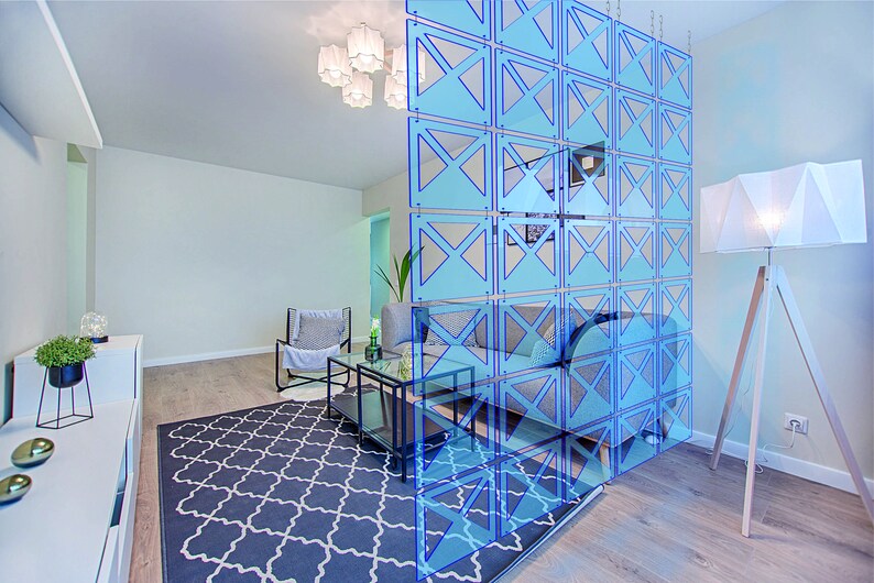 May include: A light blue room divider with a geometric pattern. The divider is made of acrylic panels and is hung from the ceiling. The divider is in front of a couch and a coffee table.