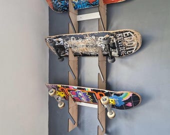 Puede incluir: Tres monopatines montados en una pared con soportes de madera. Los monopatines tienen gráficos coloridos y muestran signos de desgaste. Los soportes son de madera clara y están fijados a una pared gris.