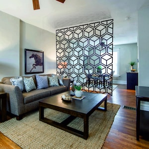 May include: A living room with a brown couch, a coffee table, and a geometric room divider. The room has a rug, wood floors, and a television on a stand.