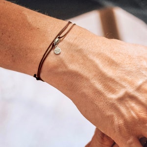 Peut inclure: Un bracelet en cordon de cuir marron avec un petit charme argenté qui dit "Nato Cuff".