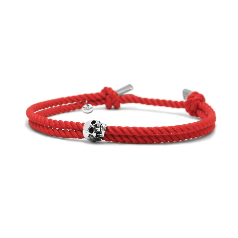 May include: Red rope bracelet with a silver skull charm. The bracelet is tied with a knot on each end.