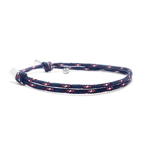 Peut inclure: Un bracelet en corde bleu marine avec des accents rouges et blancs. Le bracelet a un fermoir argenté et une petite étiquette argentée.