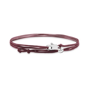 Puede incluir: Un brazalete de cordón ajustable de tres hebras de color marrón con un cierre plateado y una pequeña etiqueta plateada que dice "NATO CUFF".