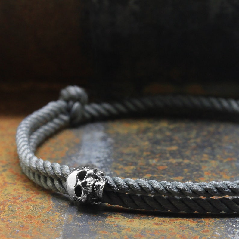 May include: A gray rope bracelet with a silver skull charm.