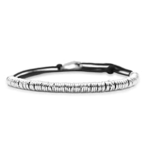 May include: A silver bracelet with a series of small, round, metallic beads strung together. The beads are connected by a black cord, and the bracelet has a silver clasp. The bracelet is displayed against a white background.