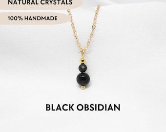 May include: A gold-toned chain necklace featuring a pendant with a small gold bead, a faceted black obsidian bead, and a larger smooth black obsidian sphere. The image includes the text NATURAL CRYSTALS, 100% HANDMADE, and BLACK OBSIDIAN.